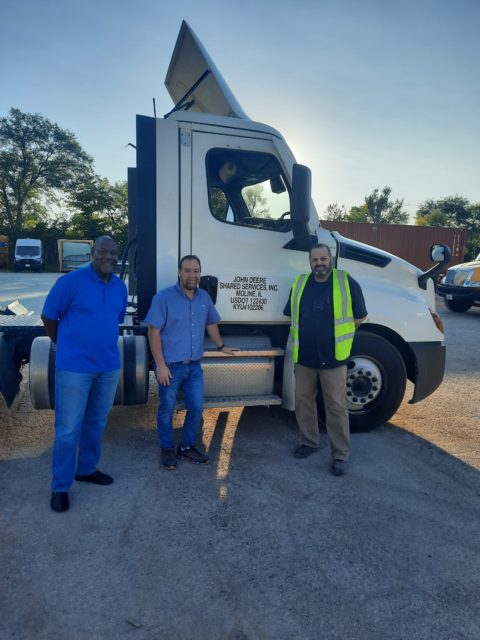 Three men stand in front of a truck.