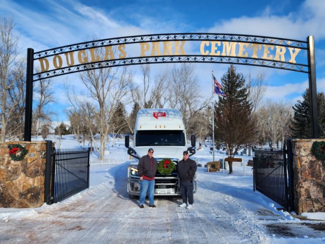 Two men stand in front of their truck underneath a Douglas Park Cemetery sign