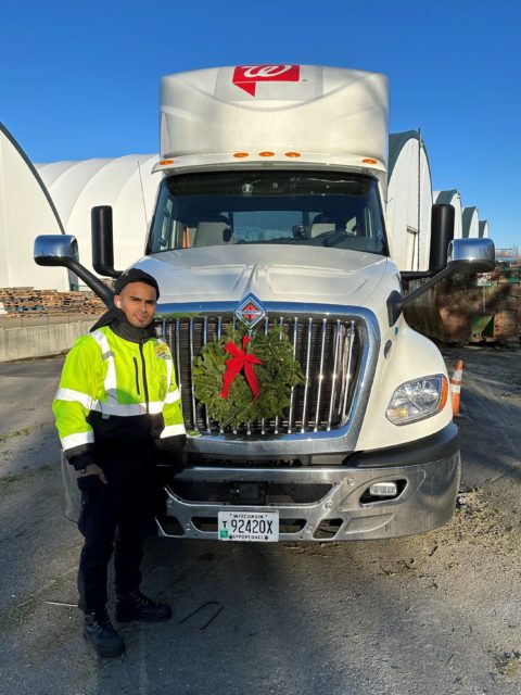A man stands in front of a truck with a wreath on the grill