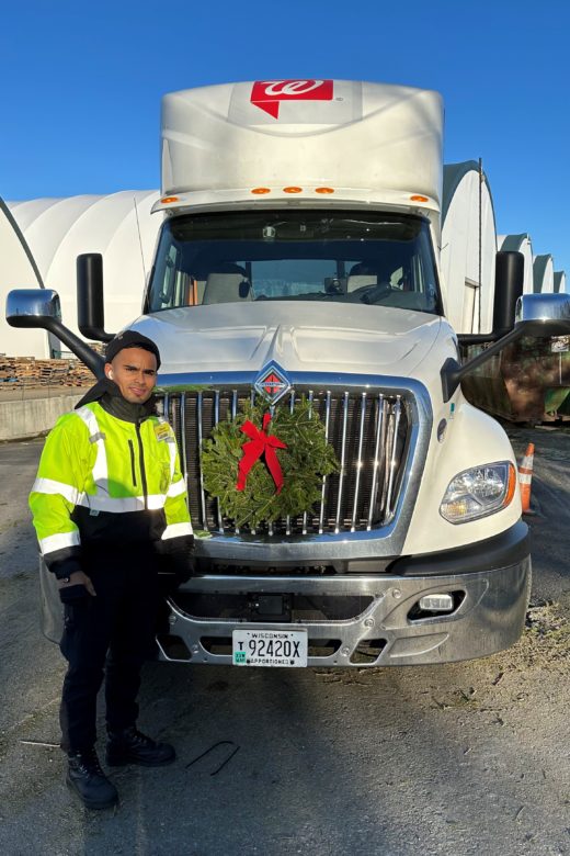 A man stands in front of a truck with a wreath on the grill