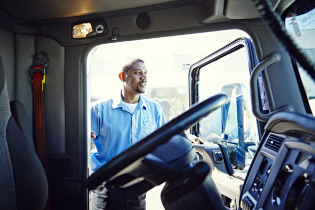 A truck driver stands in the open door of his cab.