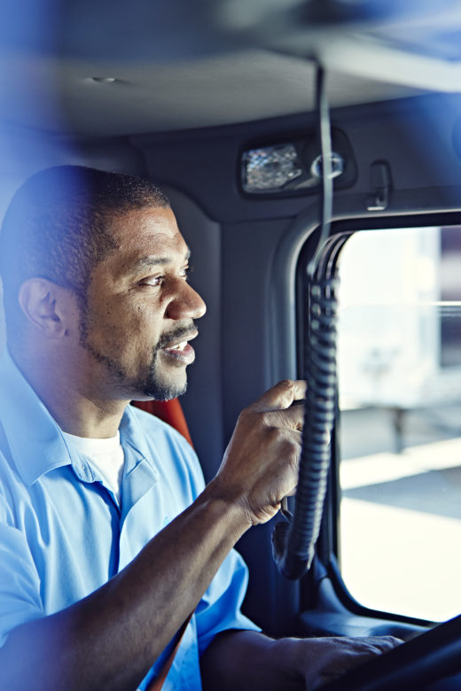 A truck driver looks out the window of his truck while holding a radio