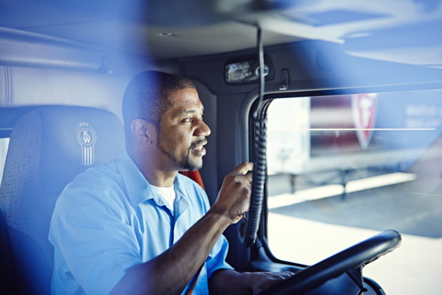 A truck driver looks out the window of his truck while holding a radio