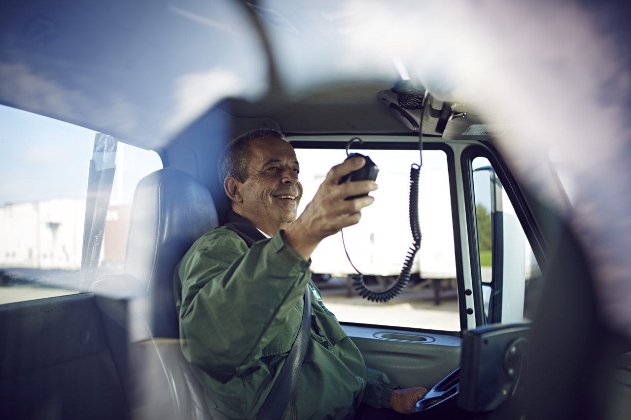 A man smiles as he grabs a radio while sitting in the driver's seat of a truck