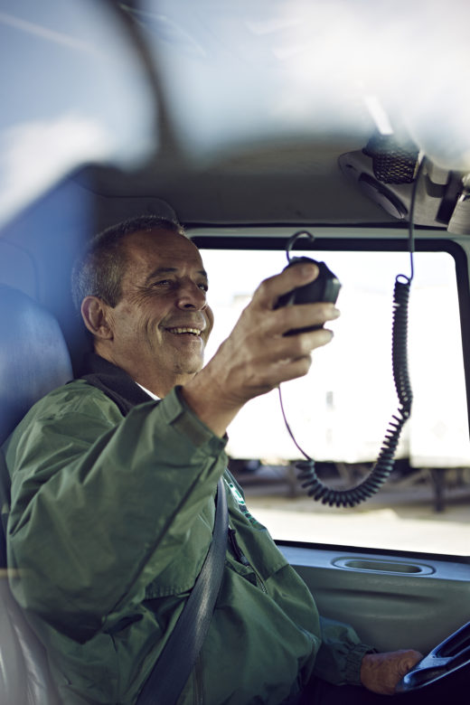 A man smiles as he gabs a radio while sitting in the driver's seat of a truck