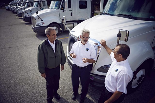 Three men stand and talk in front of a truck
