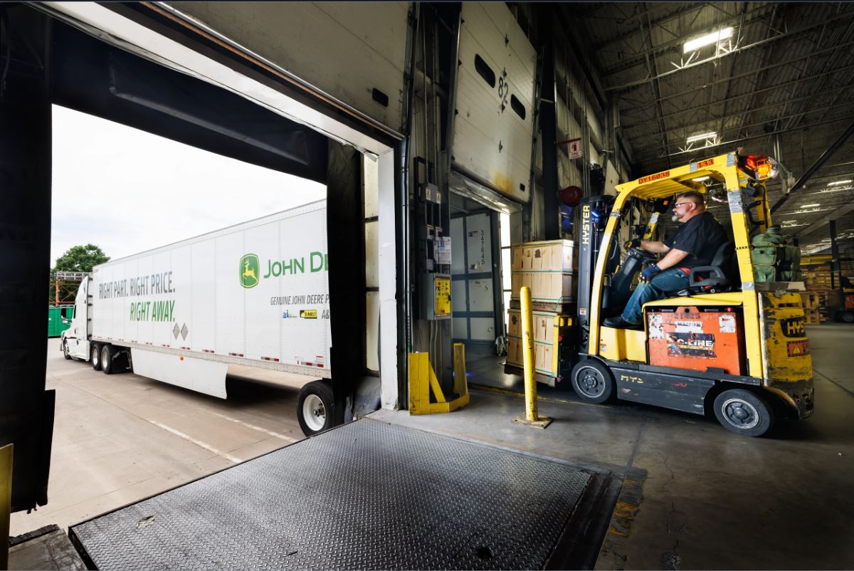 A man loads boxes into a Joh Deere truck from a warehouse.
