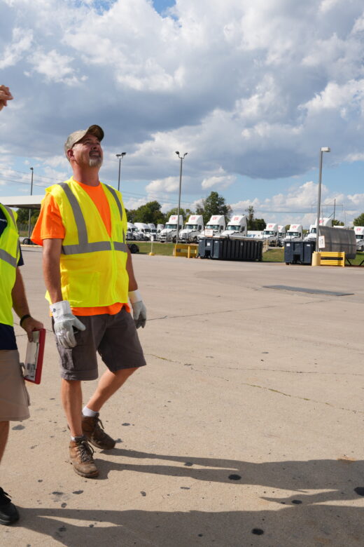 Two men walk around a parking lot while one points up.