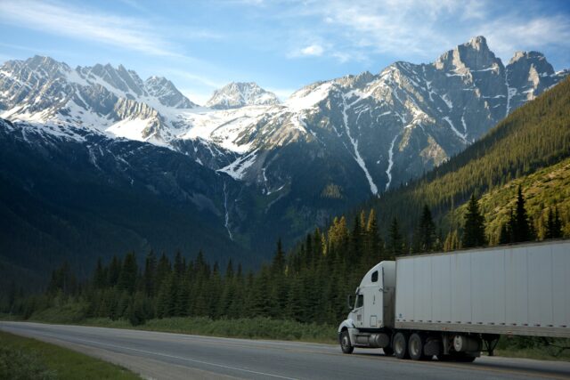 A truck drives down the road with a mountain range in the background.