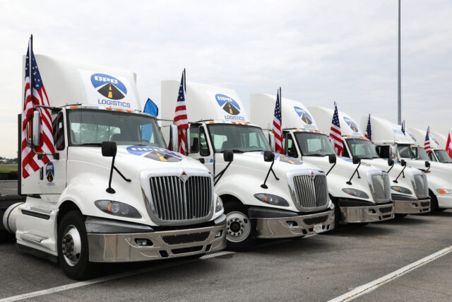 A row of trucks with American flags attached sit in a parking lot