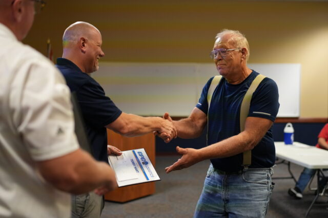 Two men shake hands while one presents the other with a certificate