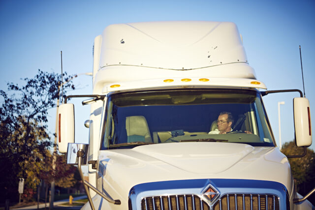 A man inside a white semi-truck glances to his left