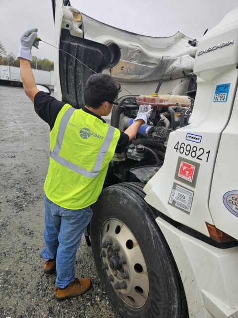 A man wearing a green vest performs maintenance work on his semi-truck.