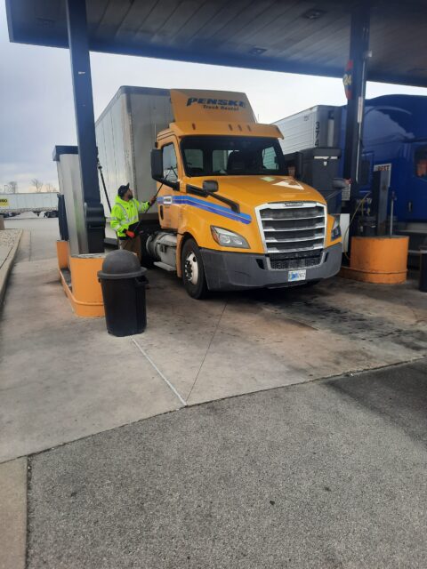 A truck driver cleans the windshield of his truck at a gas station.