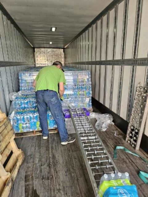 A man stands in the trailer of a semitruck unloading bottled water