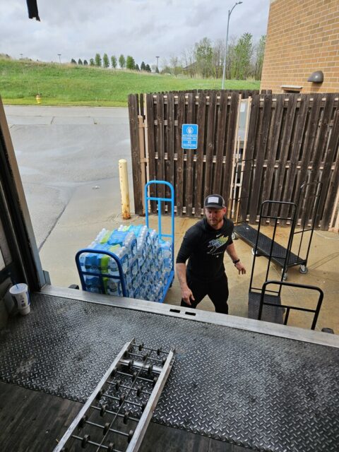 A man stands behind a semitruck trailer to unload bottled water