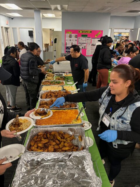 People stand in line waiting to be served food from a buffet.