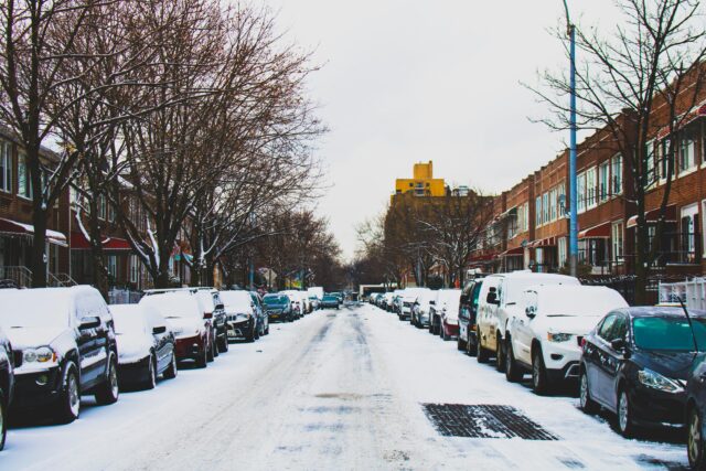 A snowy street with cars parked along the sides.