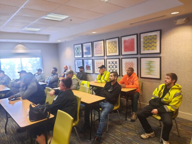 A group of truck drivers sit in rows in a classroom