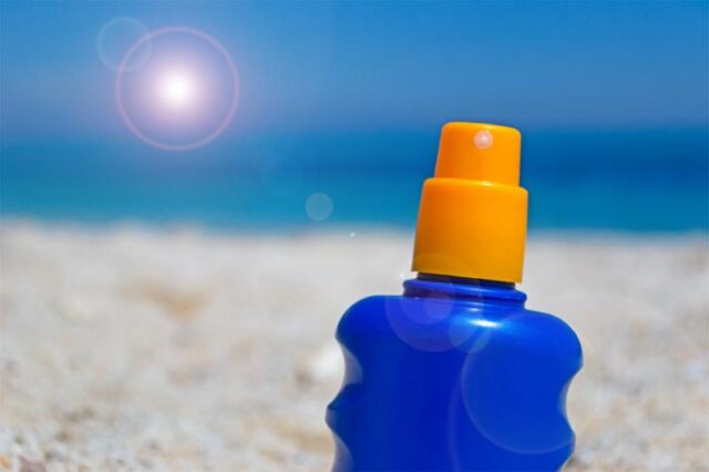 A blue bottle of sunscreen with an orange cap sits on a sunny beach.
