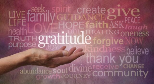 An outstretched hand holds the word "Gratitude" among a cloud of colorful words.
