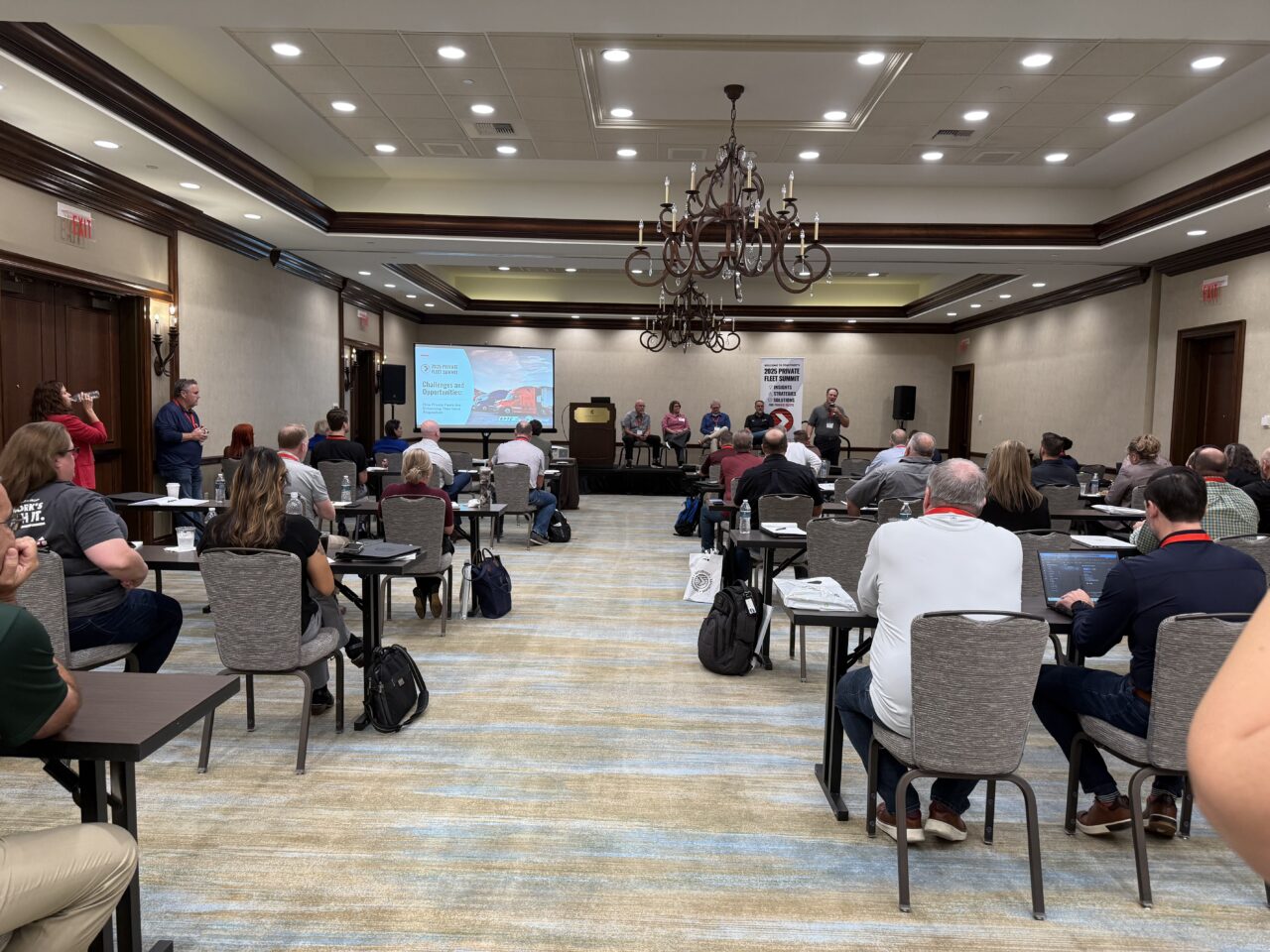 An audience watches a presentation from a group of panelists on a stage.