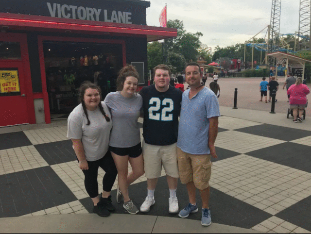 A family of four poses in front of a building with a sign that says "Victory Lane."