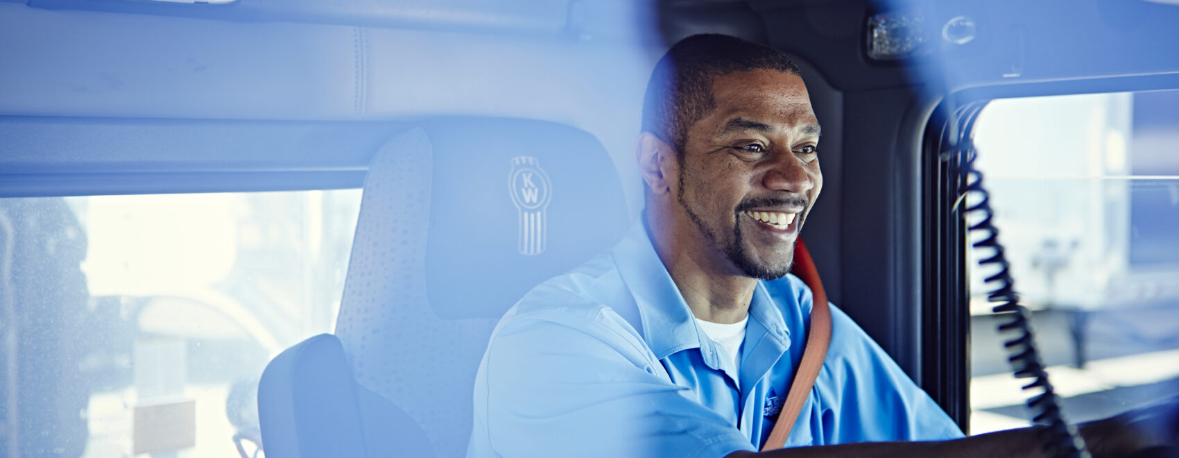 A truck driver smiles while sitting behind the wheel of his truck.
