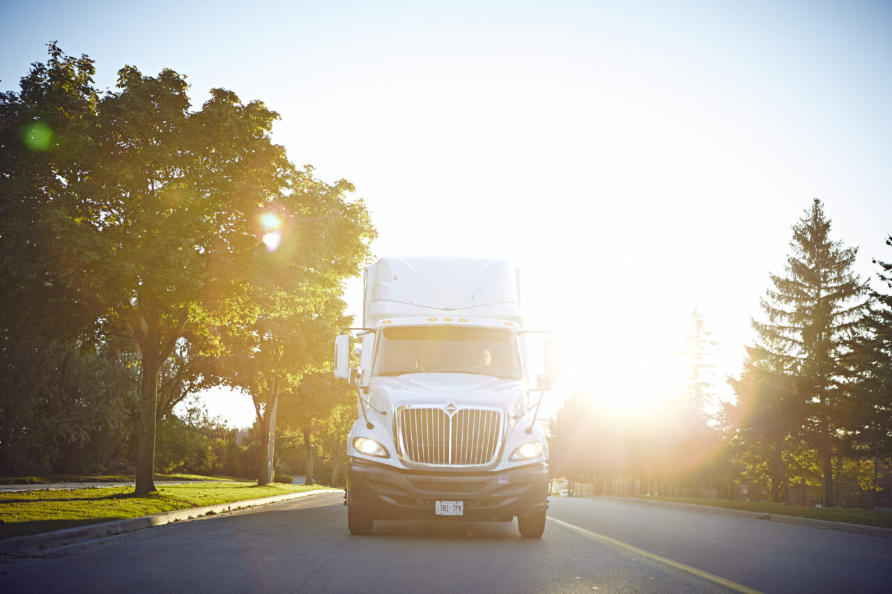 A white semi-truck drives down a road during a sunny day.