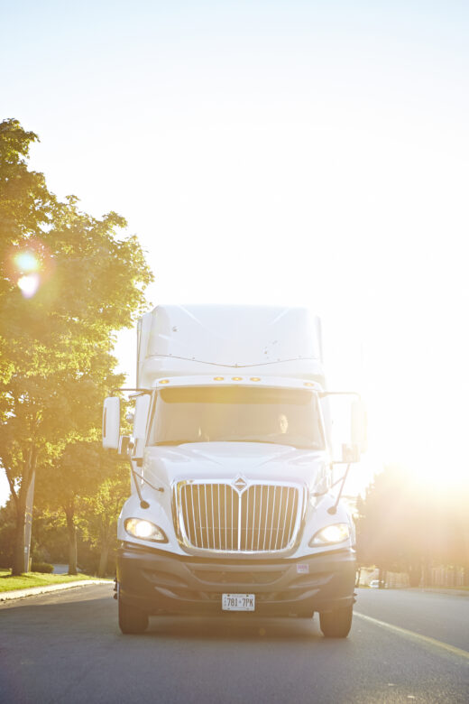 A white semi-truck drives down a road on a sunny day.