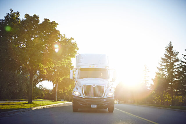 A white semi-truck drives down a road on a sunny day.
